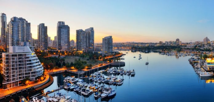 Panoramic view of a city waterfront at dusk, with high-rise buildings boasting premium housing, a marina filled with boats, and calm water reflecting the sky.