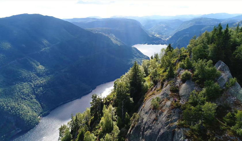 Aerial view of a mountainous landscape perfect for walking holidays in Europe, with a river winding through dense forests and rocky cliffs under a partly cloudy sky.