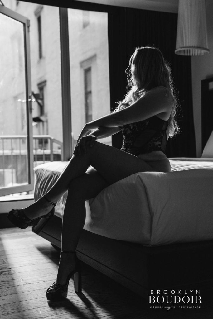 full body shot of a lady sitting on a bed looking out the window