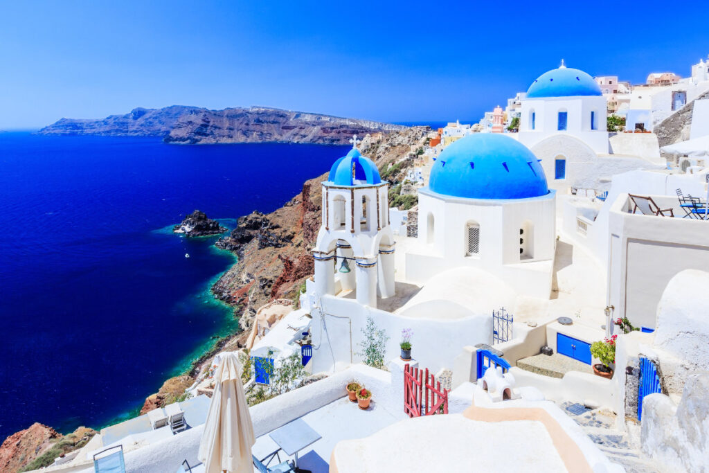 Experience one of the best places to visit with a scenic view of white buildings and blue domes overlooking the deep blue sea and cliffs in Santorini, Greece, on a sunny day.